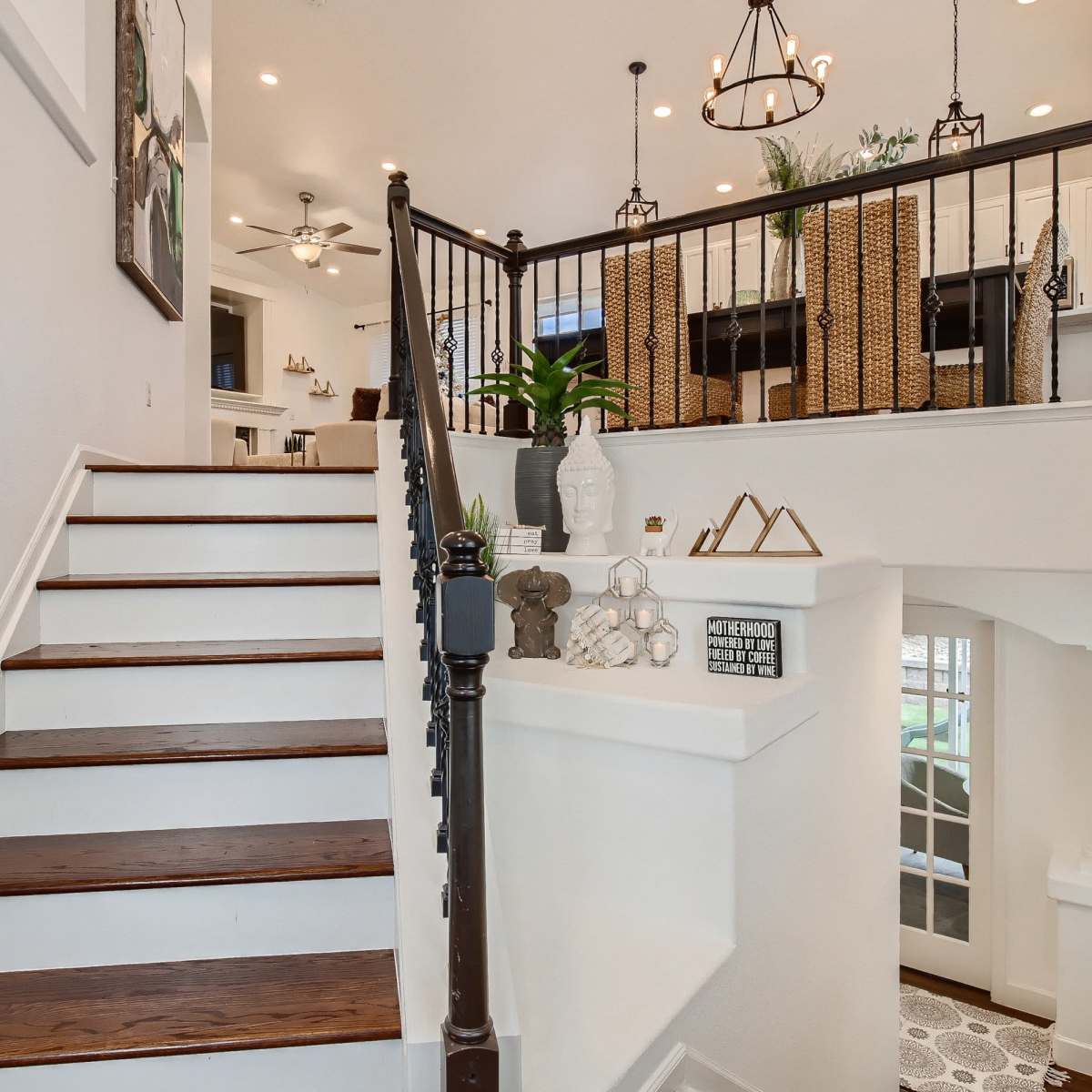 A well-lit staircase with wooden steps leading up to a landing, featuring a modern railing and decorative plants in a bright foyer.