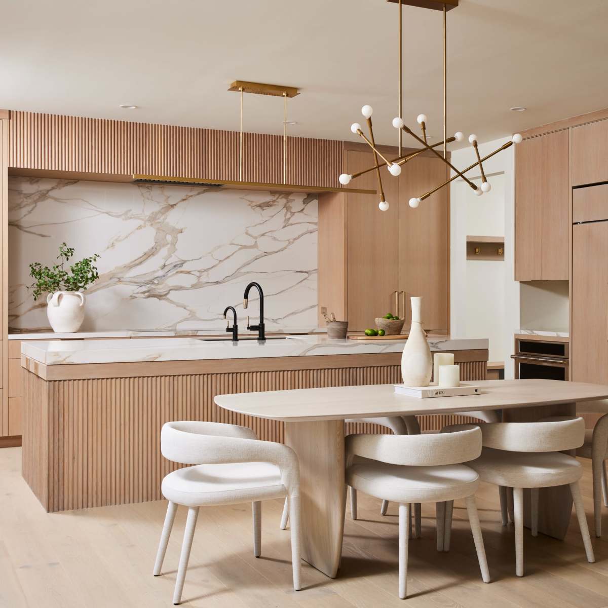 A modern kitchen with a marble countertop, wooden cabinetry, and a round dining table surrounded by upholstered chairs.