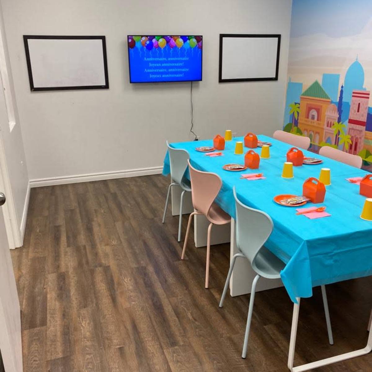 A brightly colored party room features a table set with plates and cups, with a television displaying decorations on one wall.