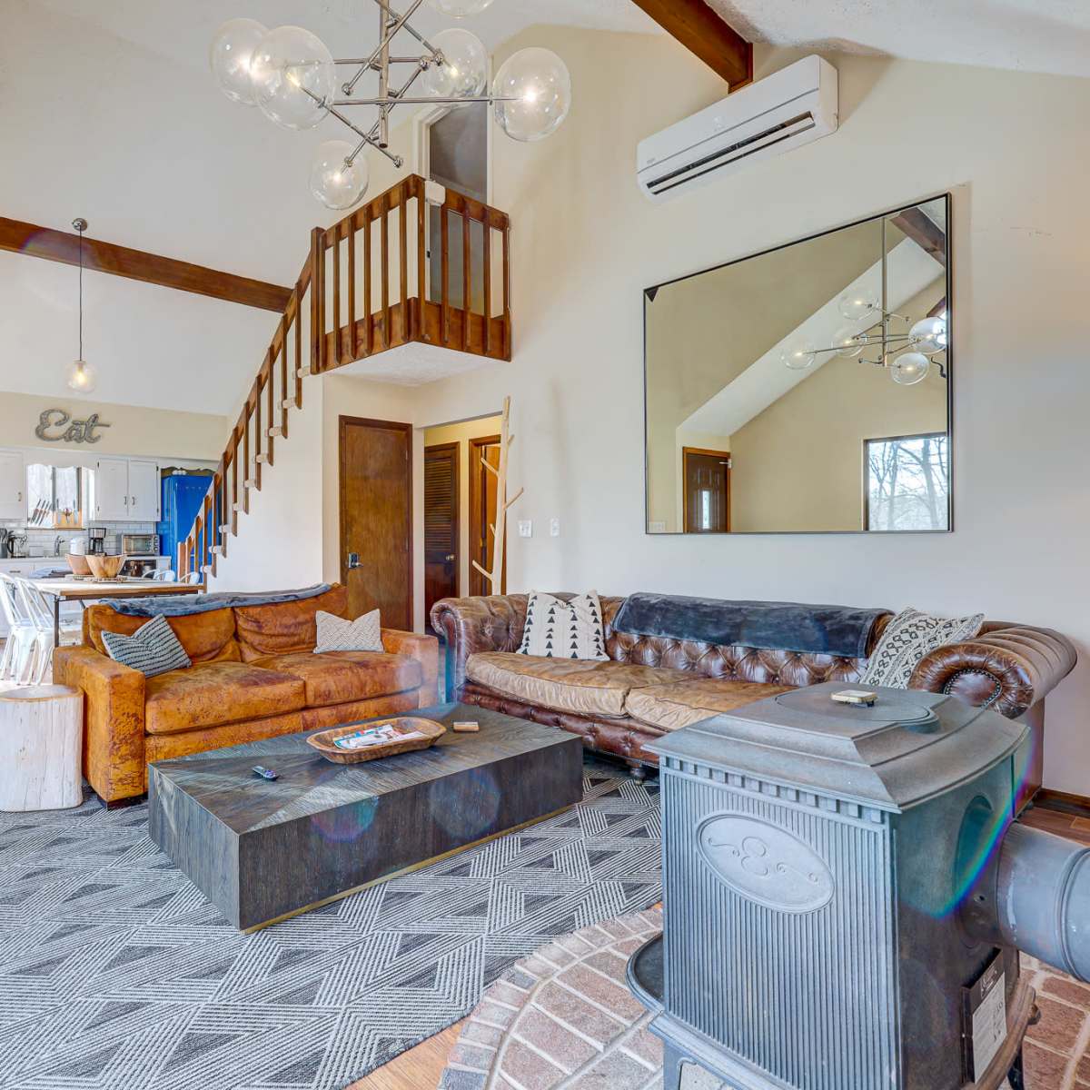 A cozy living room with a mix of modern and rustic furnishings, featuring a leather sofa, a coffee table, and a staircase leading to an upper level.