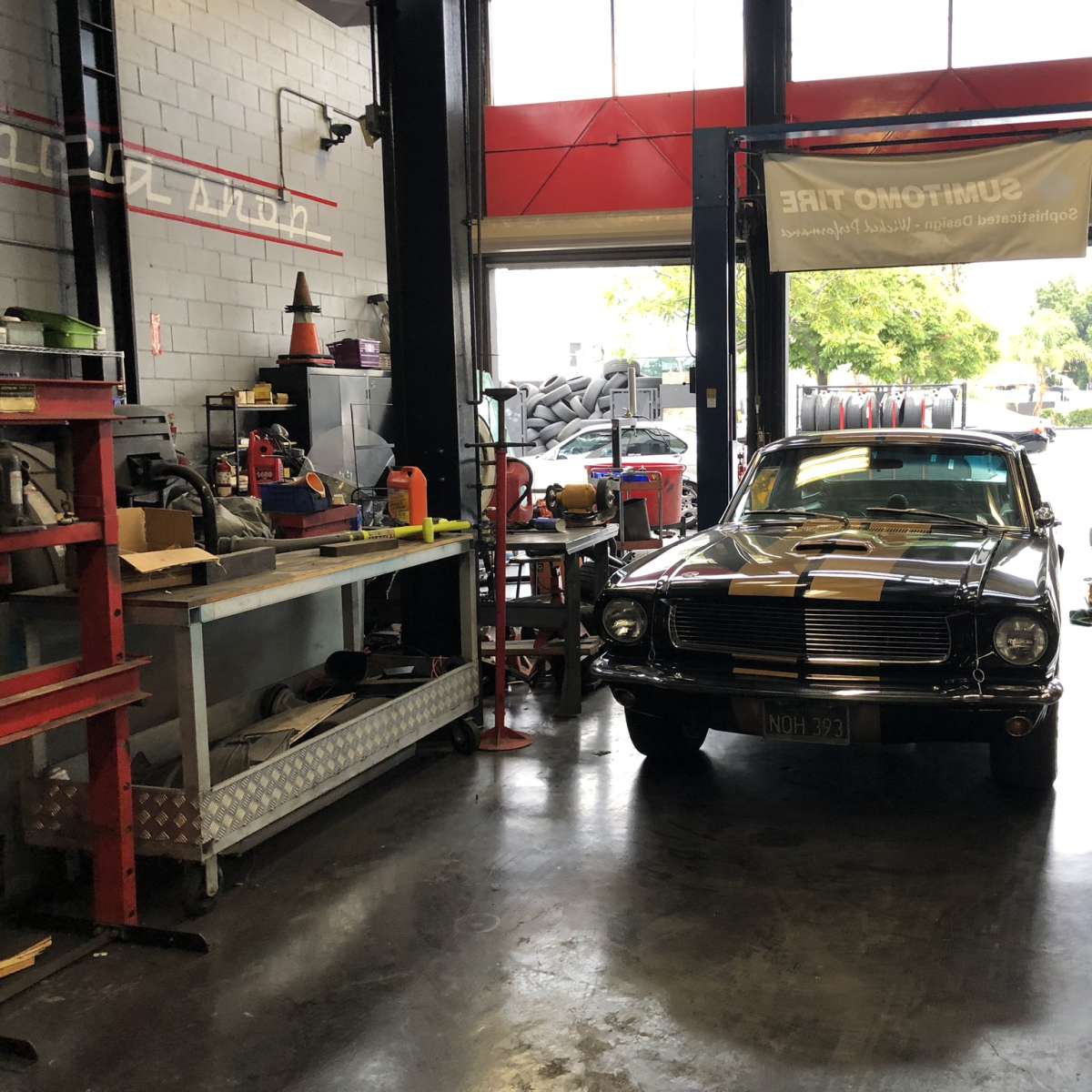 A classic car is parked inside a tire shop, surrounded by various tools and equipment along the walls.