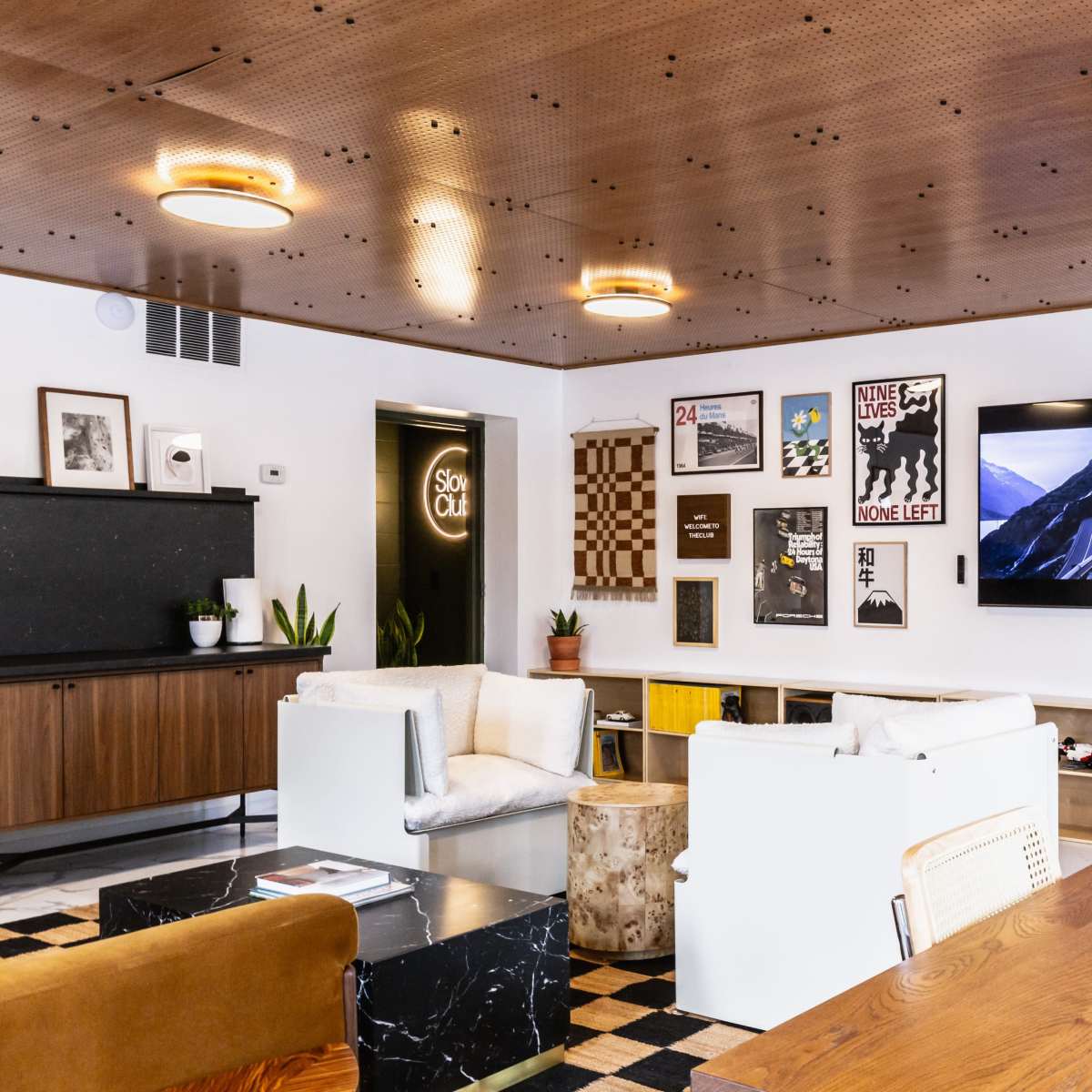 A modern lounge area featuring a television on the wall, a mix of seating options, and decor that includes artwork and plants.