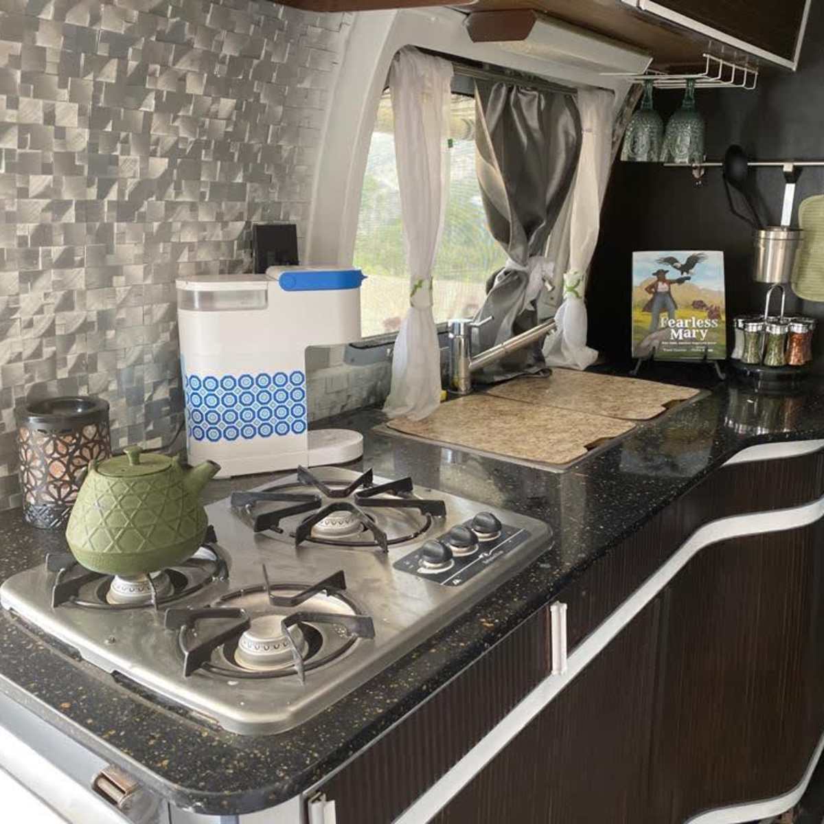 A modern kitchen with a gas stove, a green teapot, and various kitchen accessories on a countertop with a textured backsplash.