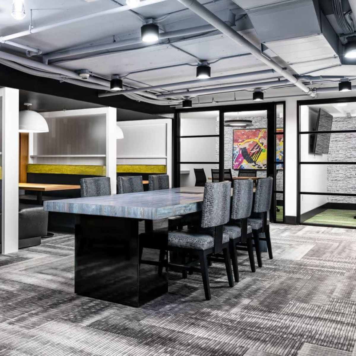 A modern workspace featuring a mix of seating areas, including booths and a large table, with stylish decor and ambient lighting.
