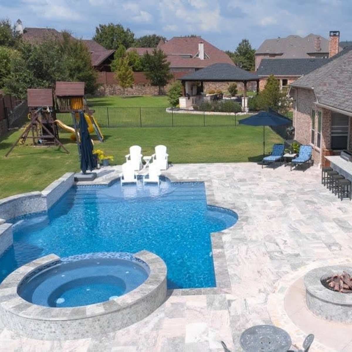A landscaped backyard with a swimming pool, a spa, and an outdoor seating area beside a large house.