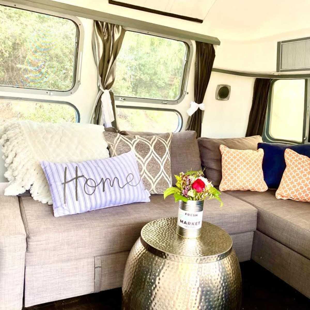 A cozy seating area features a sectional sofa adorned with decorative pillows and a small table with a floral arrangement.