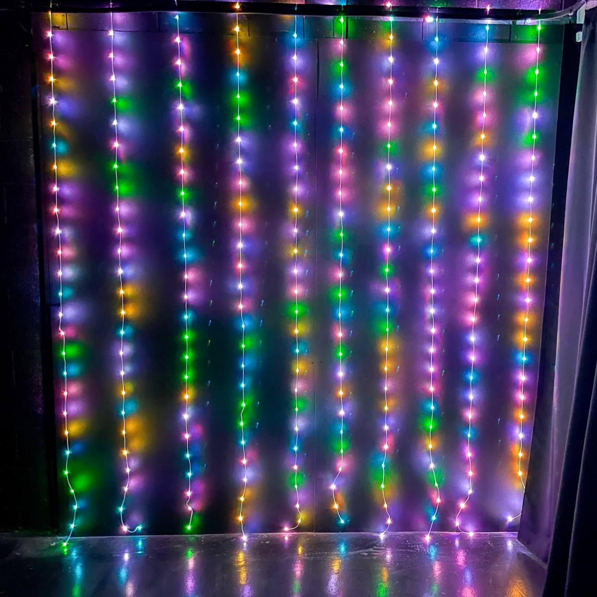 A wall covered with vertically hanging string lights in various colors.