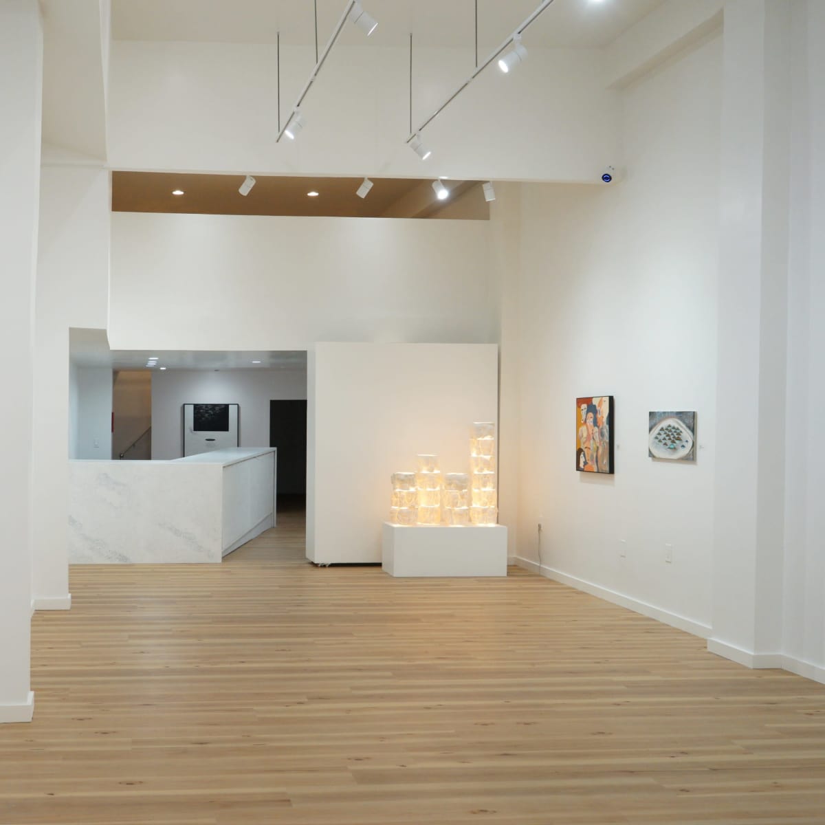 The interior of a contemporary art gallery featuring wooden flooring, white walls, and a selection of displayed artworks, including an orange construction sign.