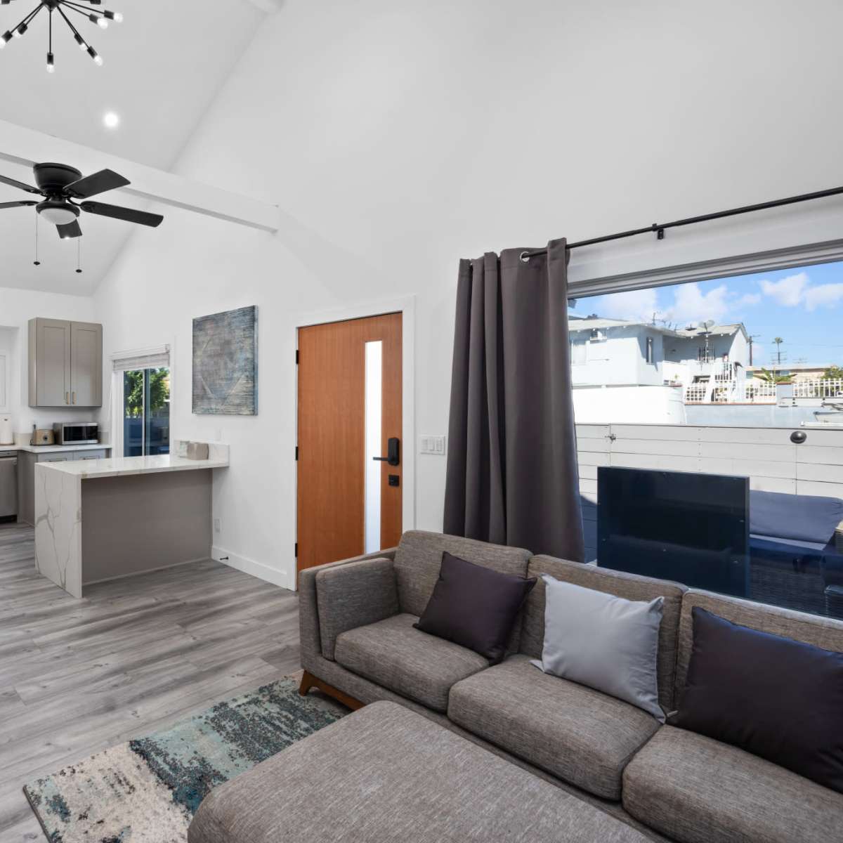 A modern, open-concept living area with a sofa, kitchen, and large windows letting in natural light.