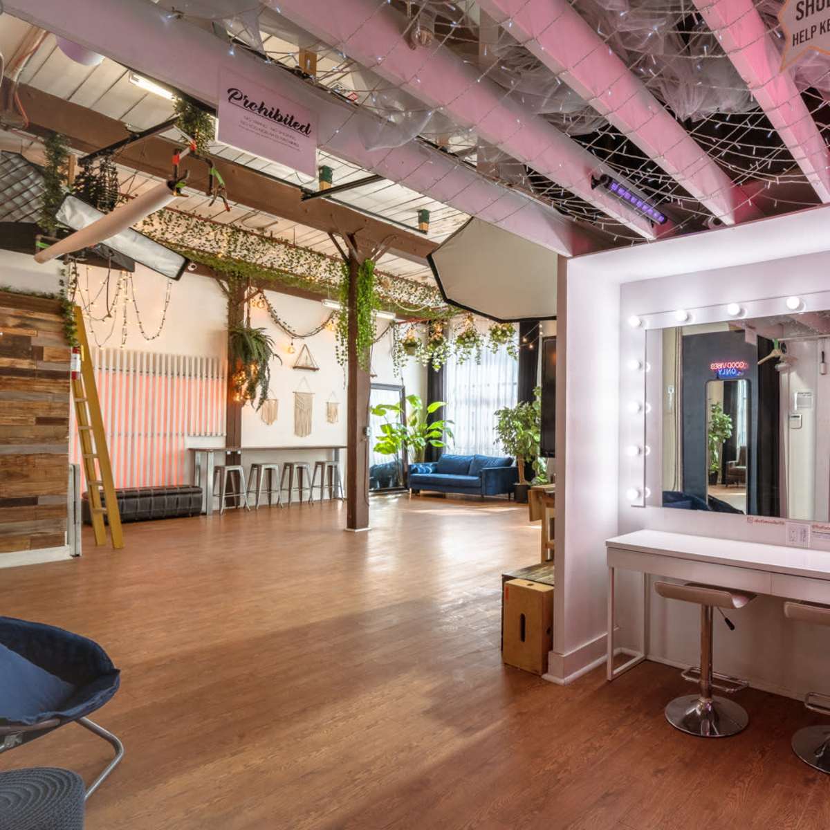 A brightly lit room with a large illuminated vanity mirror, a seating area, and decorative plants hanging from the ceiling.