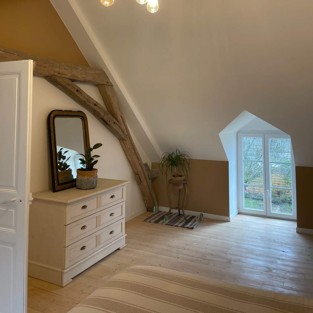 A well-lit attic bedroom featuring a dresser, a mirror, and large windows with a view.