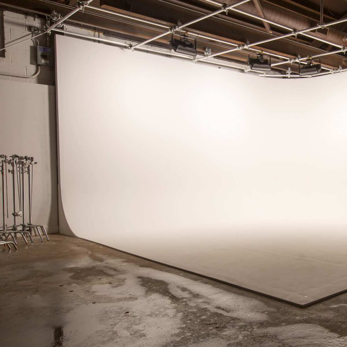 A large, empty studio space with a seamless white backdrop and concrete flooring.