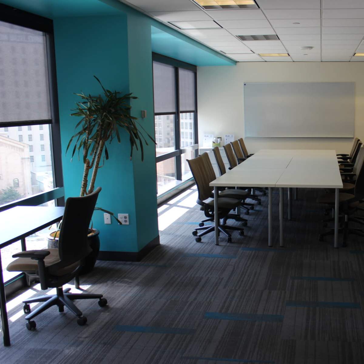 A modern conference room with a long table surrounded by chairs, large windows, and a whiteboard on one wall.