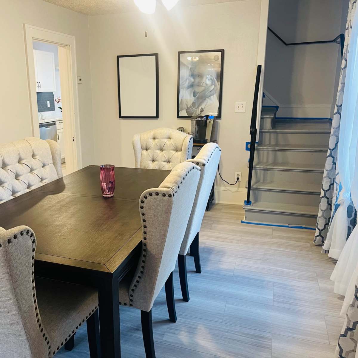 A dining area features a dark wooden table surrounded by five upholstered chairs, with a staircase visible in the background.