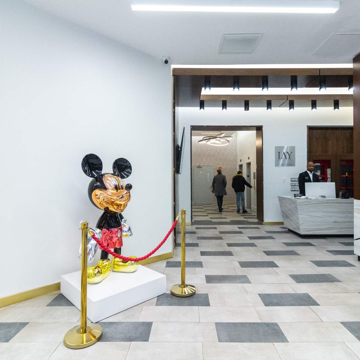 A large, colorful Mickey Mouse statue stands on a pedestal in a modern lobby with a reception area visible in the background.