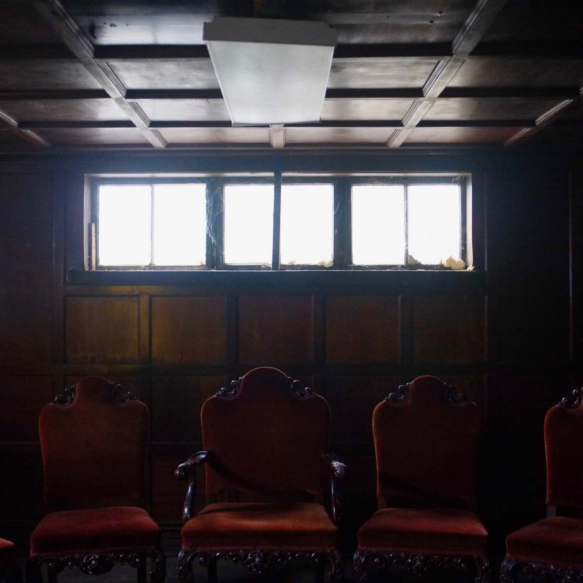 A dimly lit room with a row of ornate, upholstered chairs facing a small window.