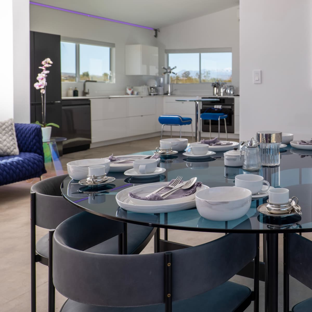 A round dining table is set with dishes and silverware in a modern kitchen and dining area.