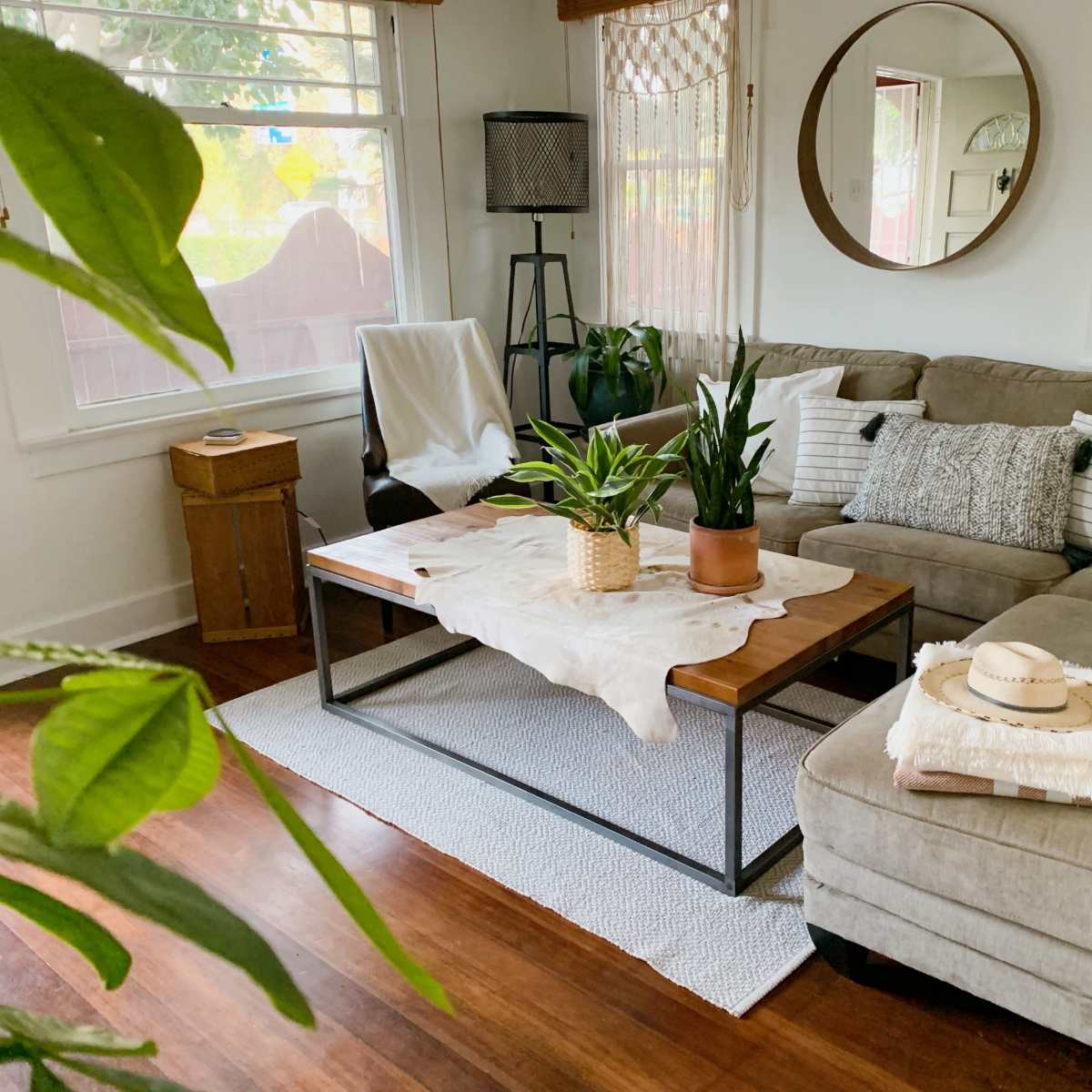 A cozy living room features a sectional sofa, a wooden coffee table with plants, and natural light coming through a window.