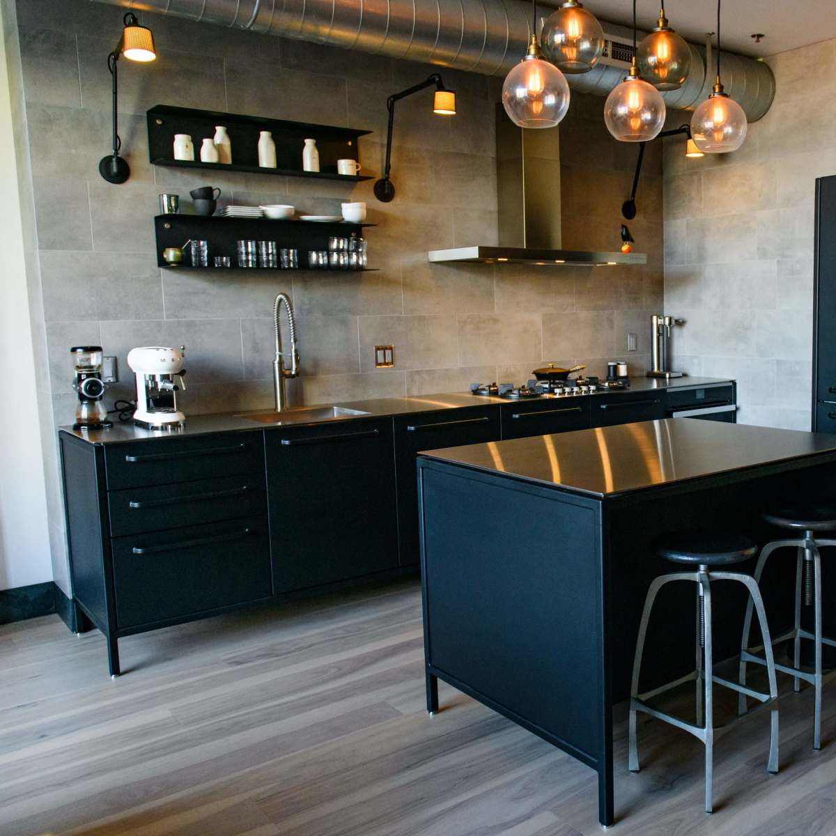 A modern kitchen featuring black cabinetry, a central island with seating, and industrial-style lighting.