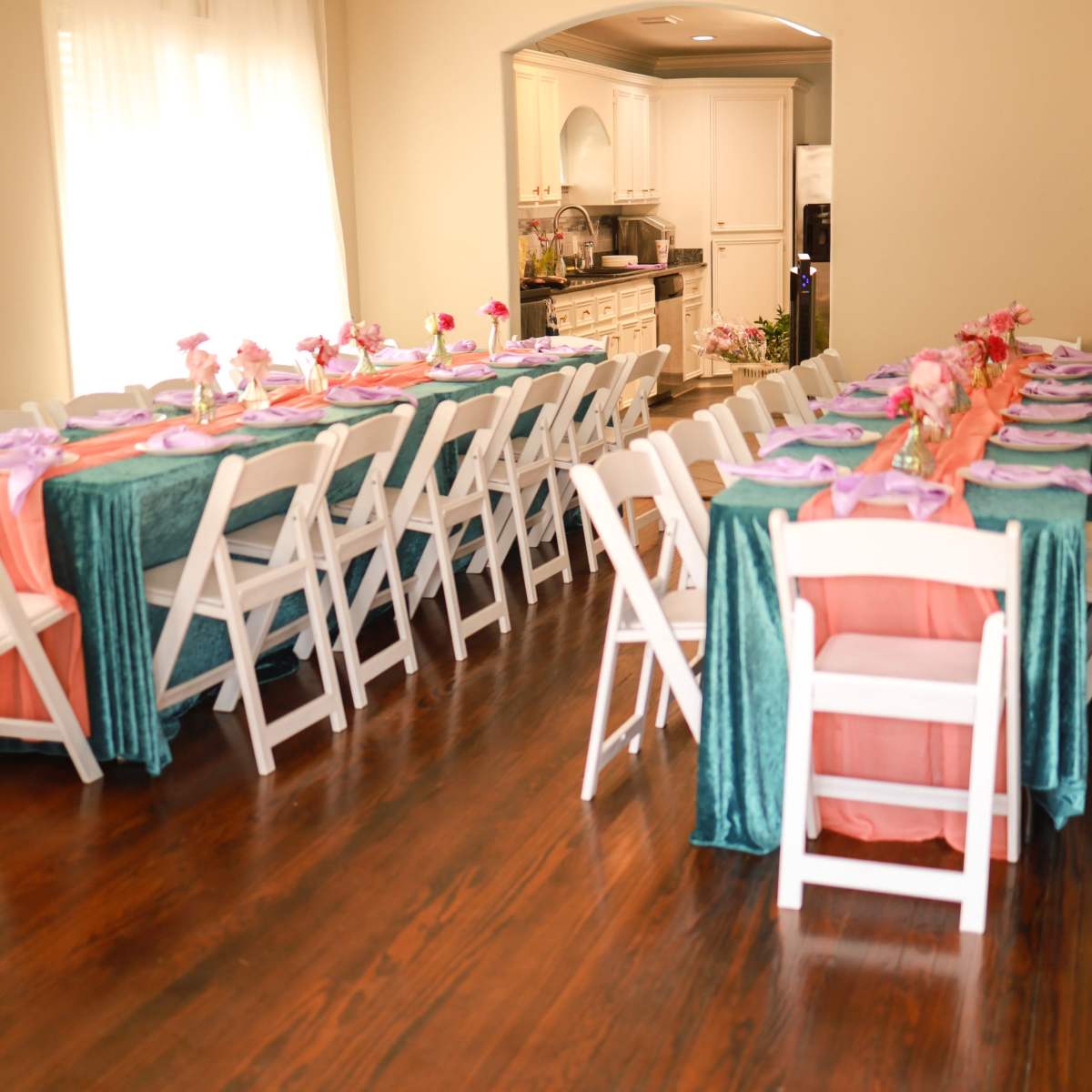 A dining area is set up with several tables covered in teal and coral tablecloths, each adorned with floral centerpieces and place settings.