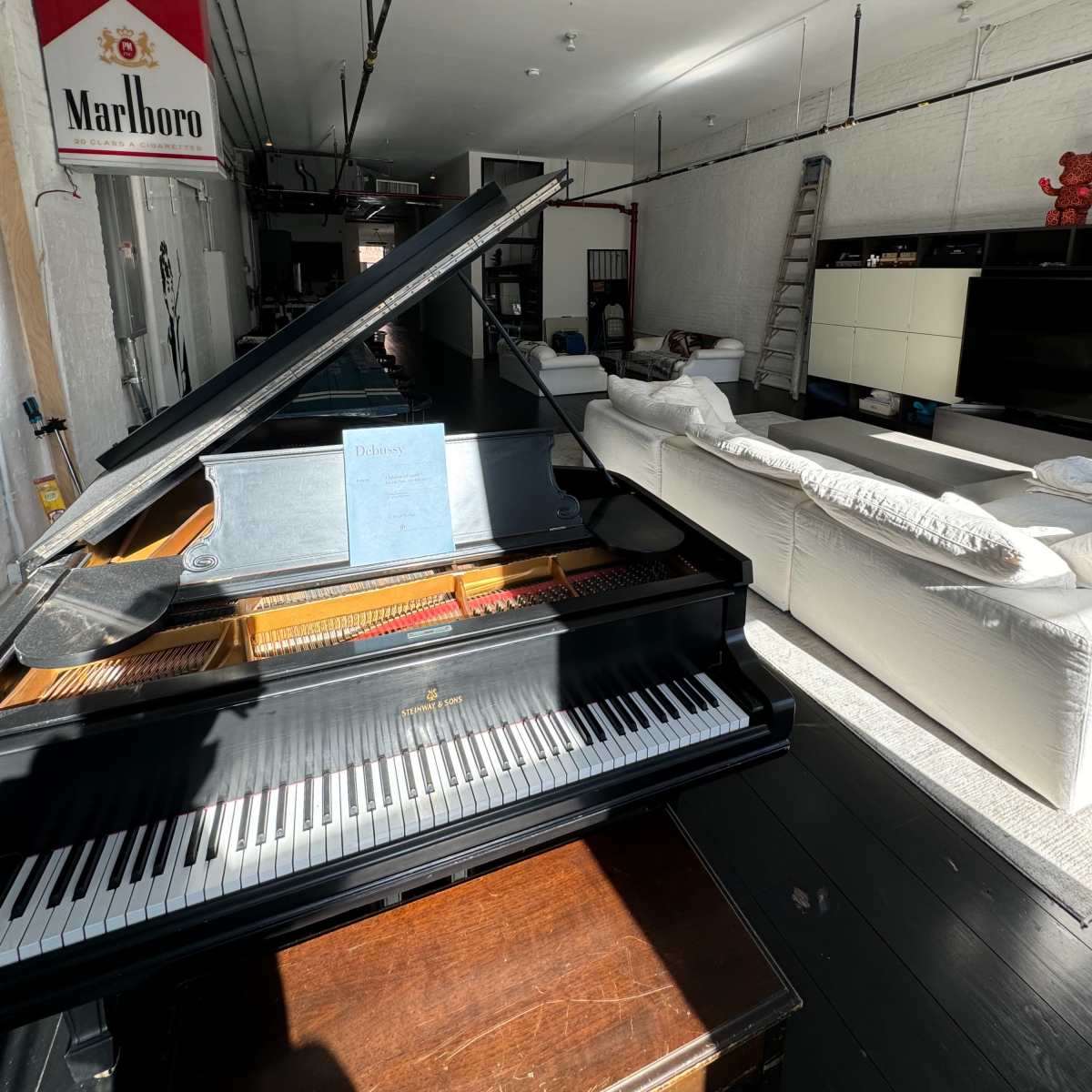 A grand piano in the foreground, with a modern living area featuring a white sofa and a large television in the background.