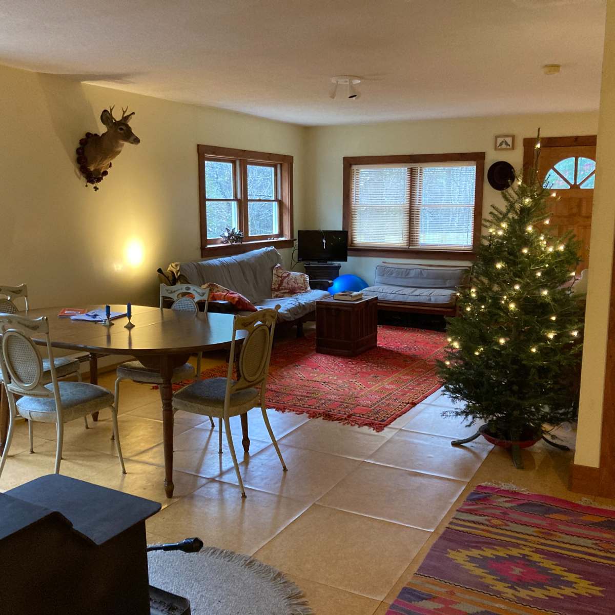 A cozy living room with a dining area, a Christmas tree, a couch, and a decorative rug on the floor.