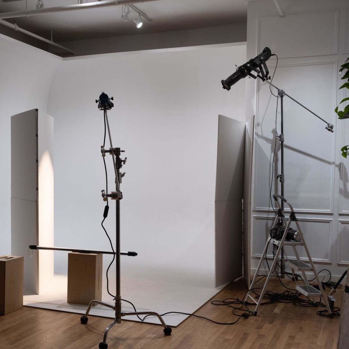 A photography studio features a curved backdrop, lighting equipment, and empty boxes on a wooden floor.