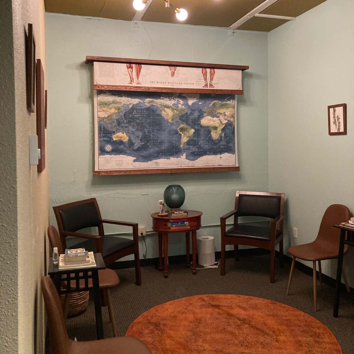 A small room with a round orange rug, four chairs, a wooden table, and a world map mounted on the wall.