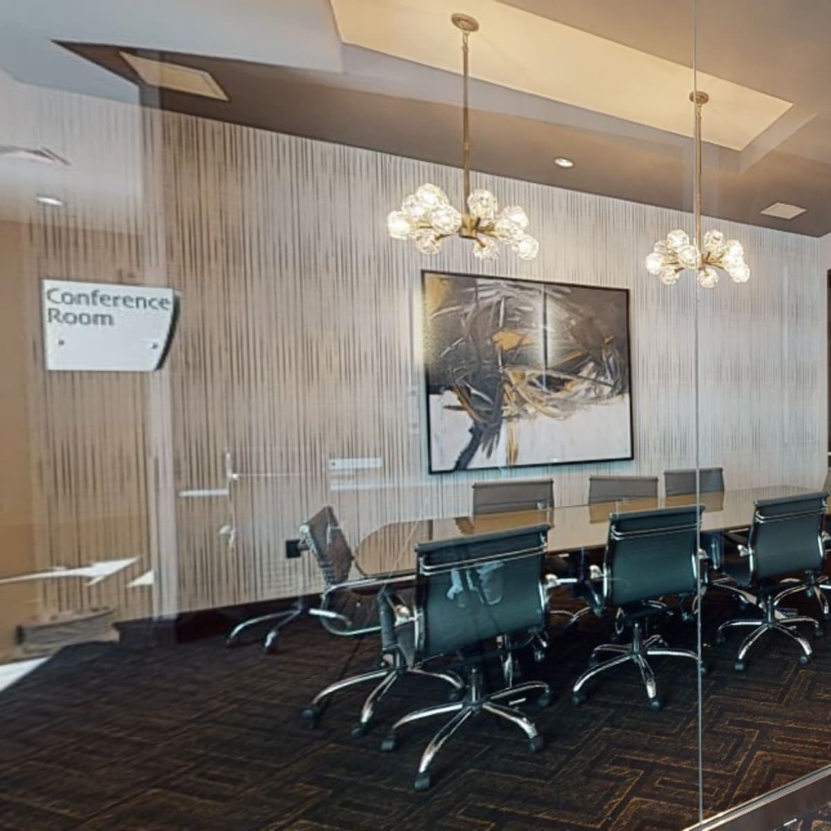 A modern conference room with a large table, black chairs, and a decorative wall featuring a television and artwork.
