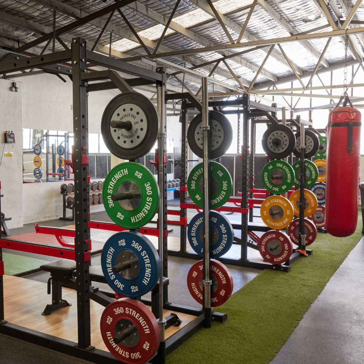 A gym interior with weightlifting equipment, including barbells with color-coded plates and a red punching bag in the background.