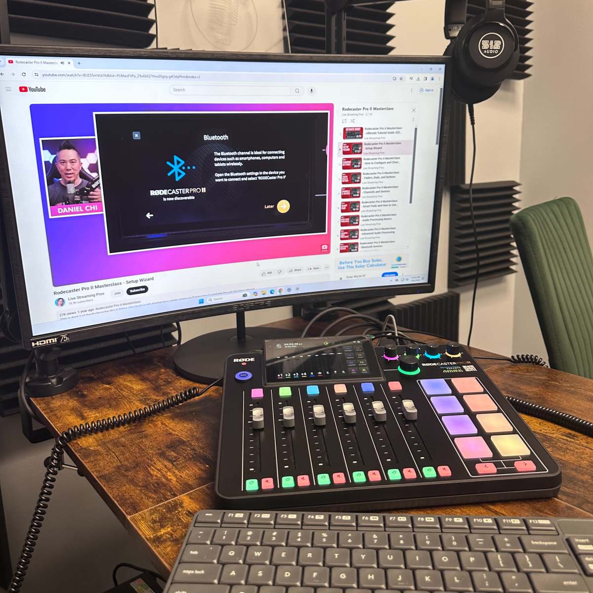 A computer monitor displaying a streaming software interface, with an audio mixer and keyboard on a wooden desk in a studio setup.