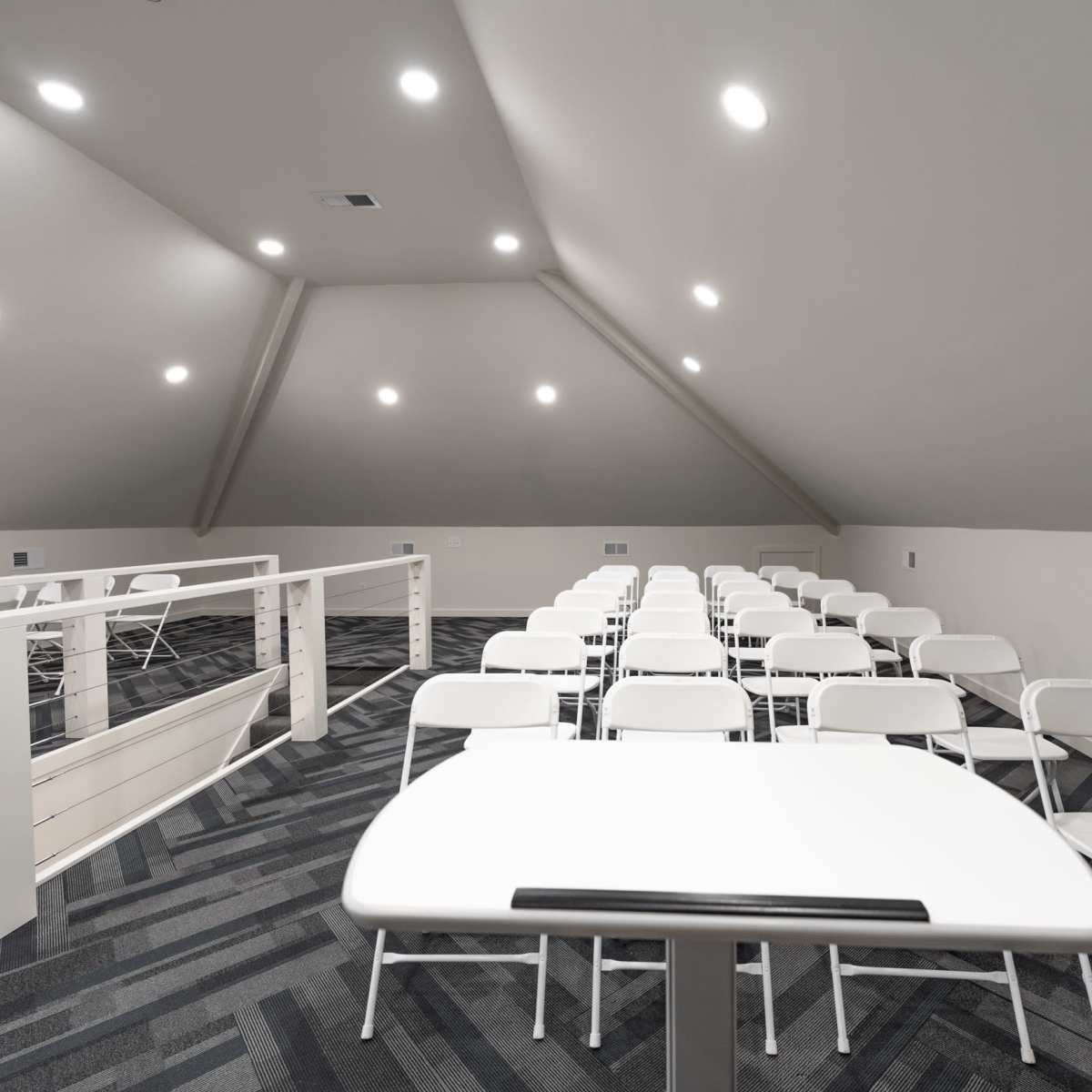 A spacious, well-lit attic room with rows of white folding chairs and tables arranged for an event.