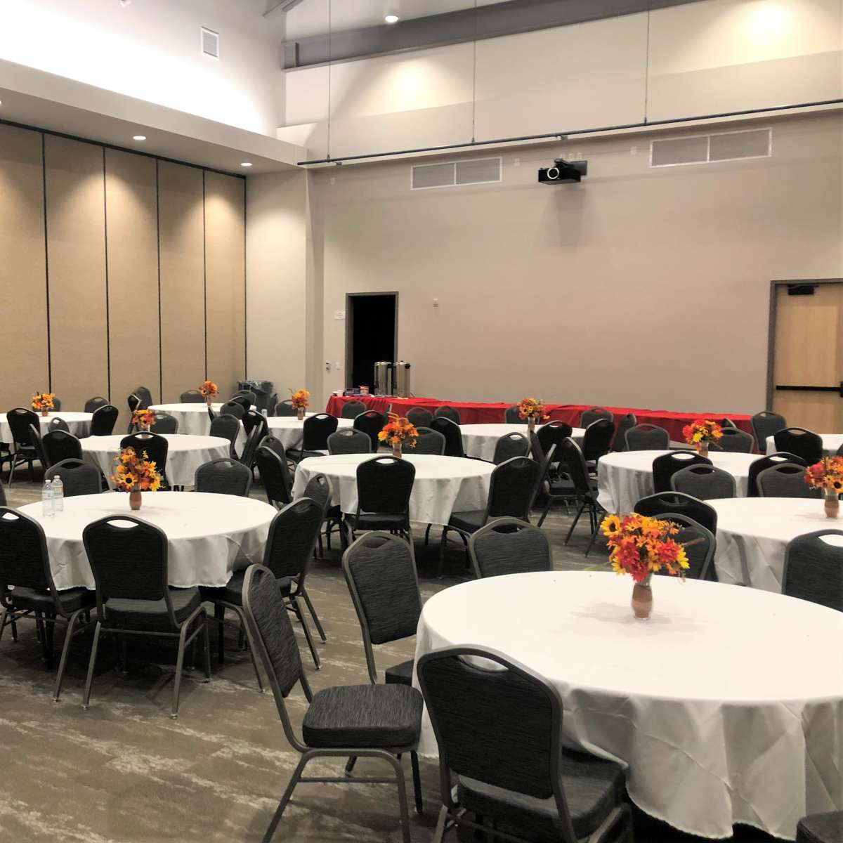 A large meeting room with round tables covered in white tablecloths and decorated with flower centerpieces, arranged in a grid pattern.
