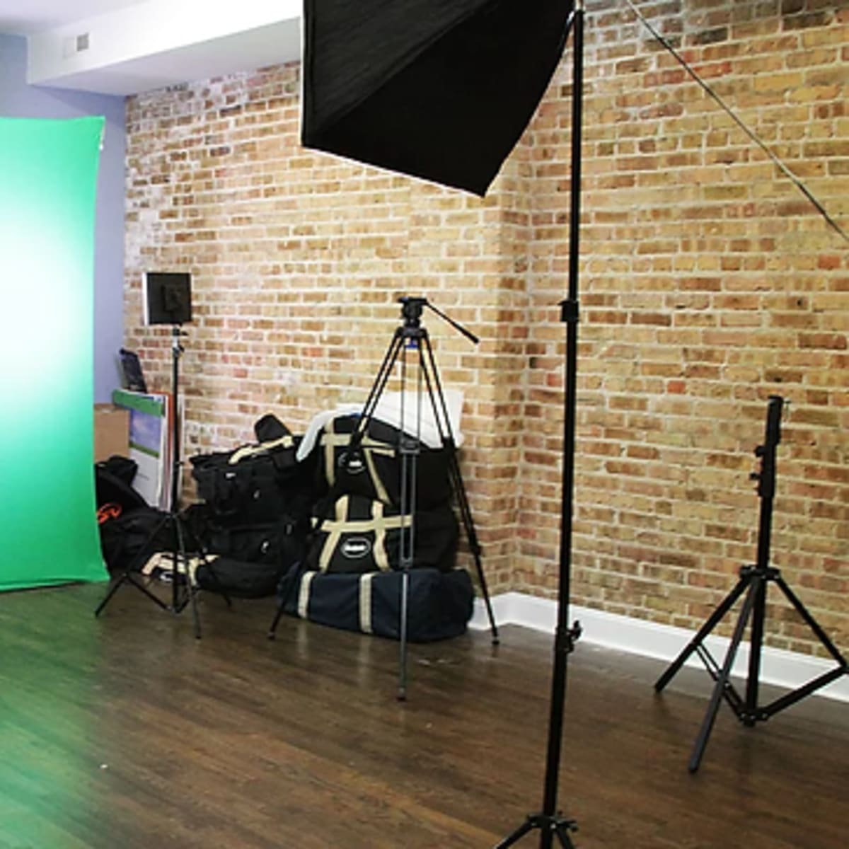 A video production setup featuring a green screen, director's chair, lighting equipment, and tripods in a studio with exposed brick walls.