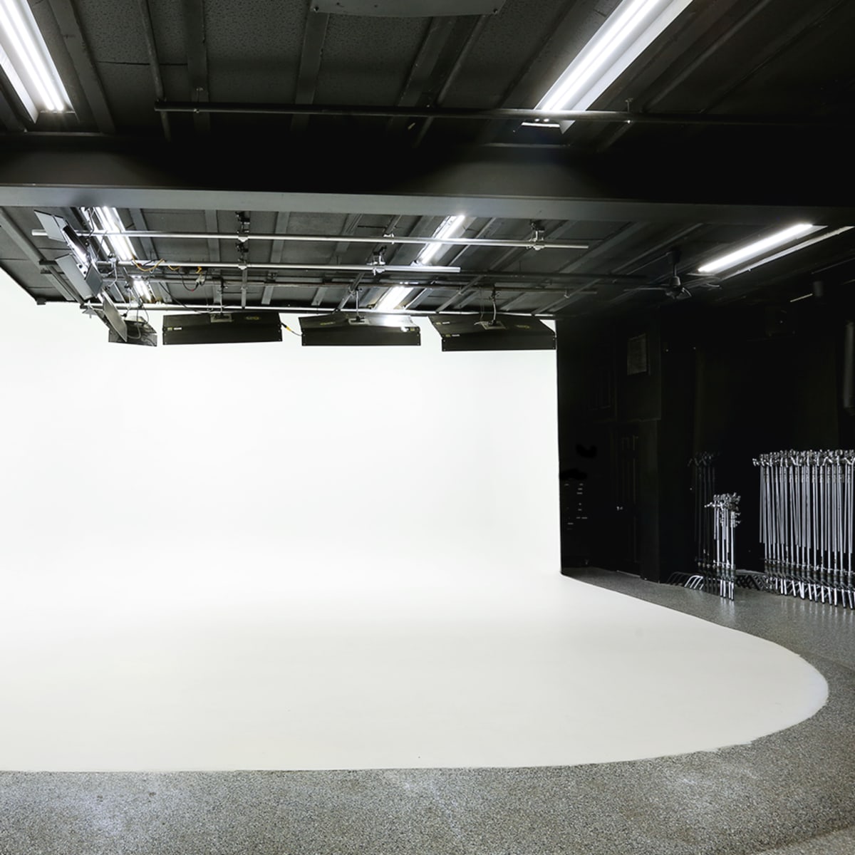 An empty studio space with a seamless white backdrop and overhead lighting.