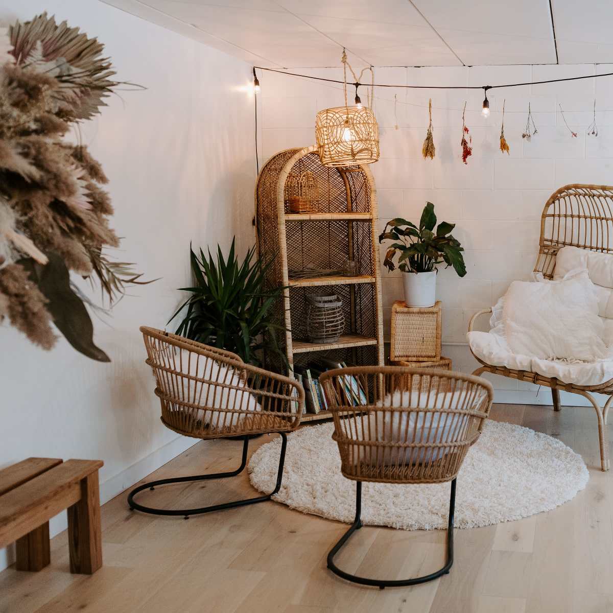 A cozy living space featuring rattan furniture, a round rug, and potted plants, illuminated by pendant lights.