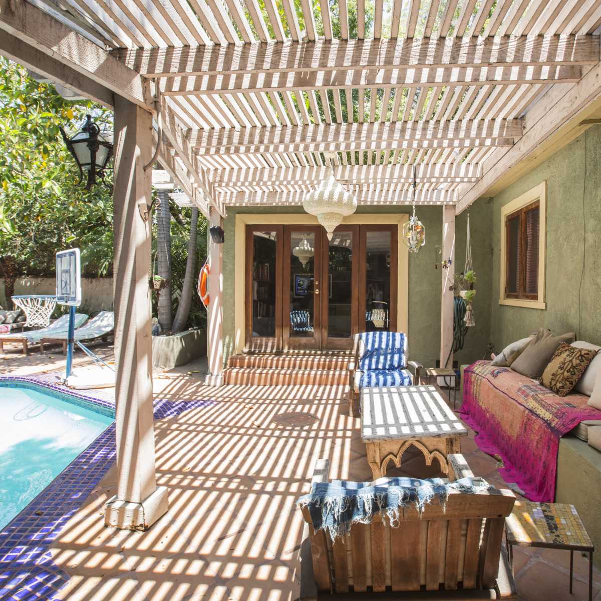 A patio area with a wooden structure overhead, a pool adjacent to it, and seating arranged along the side.