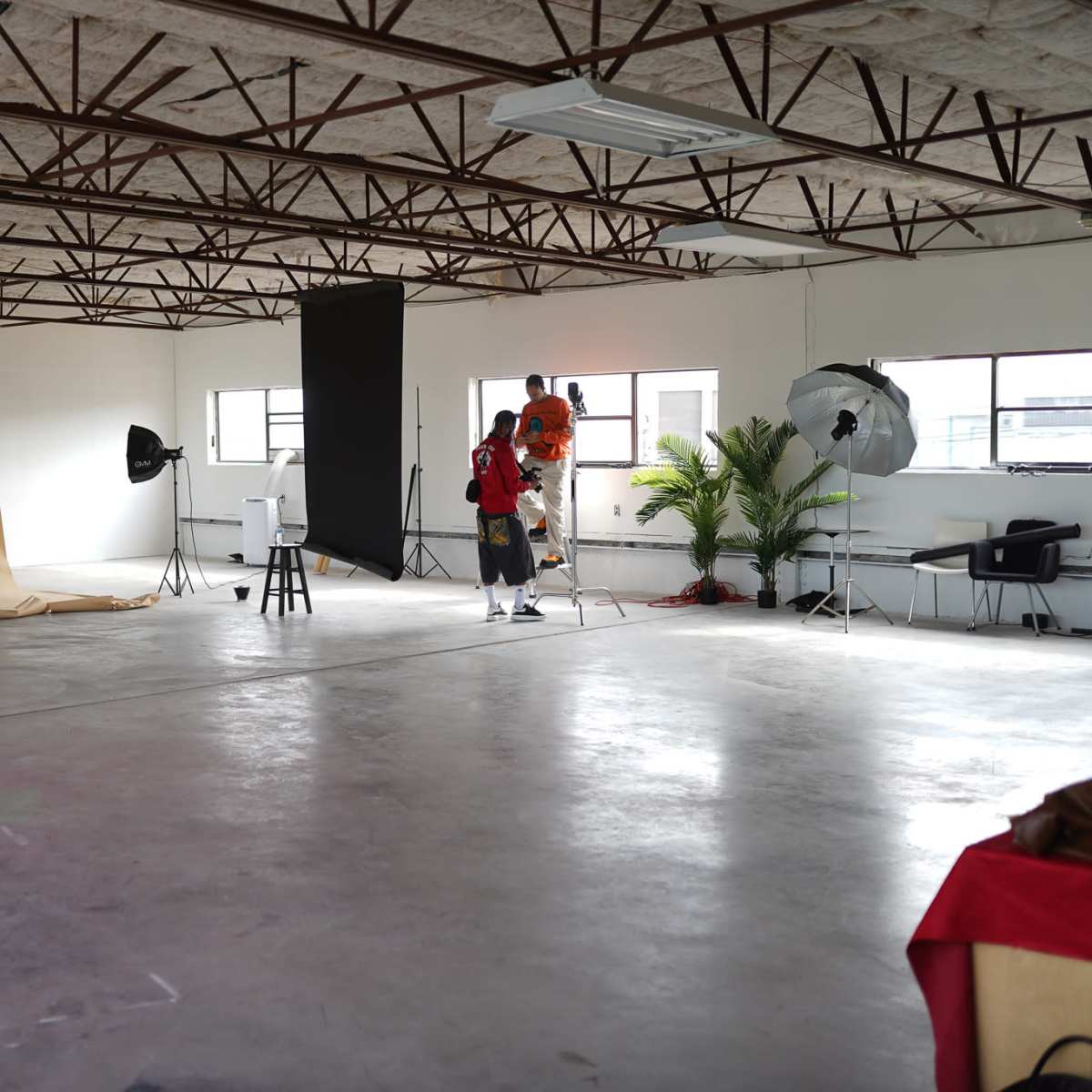 A photography studio with a large empty space, a beige backdrop, a black backdrop, lighting equipment, and a person setting up.
