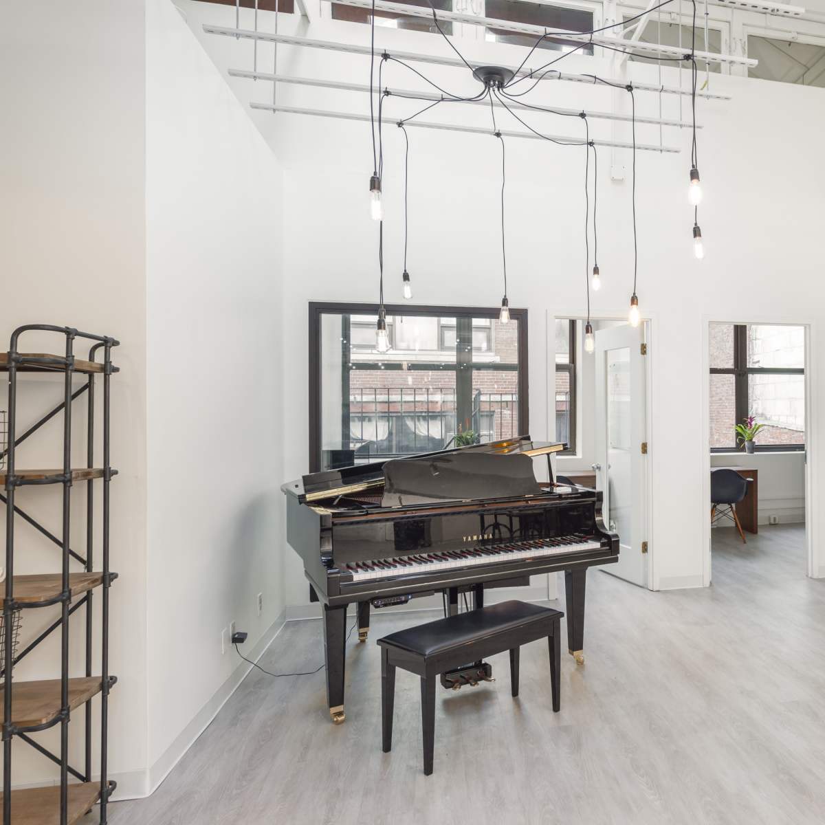 A bright room featuring a grand piano with a black stool, large windows, and modern lighting fixtures.