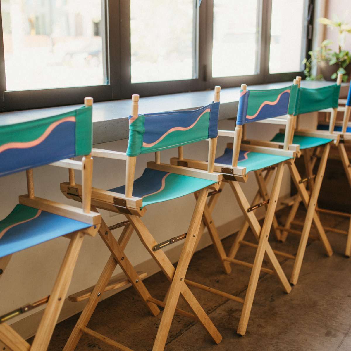 A row of wooden director's chairs with colorful canvas seats is lined up near a large window.