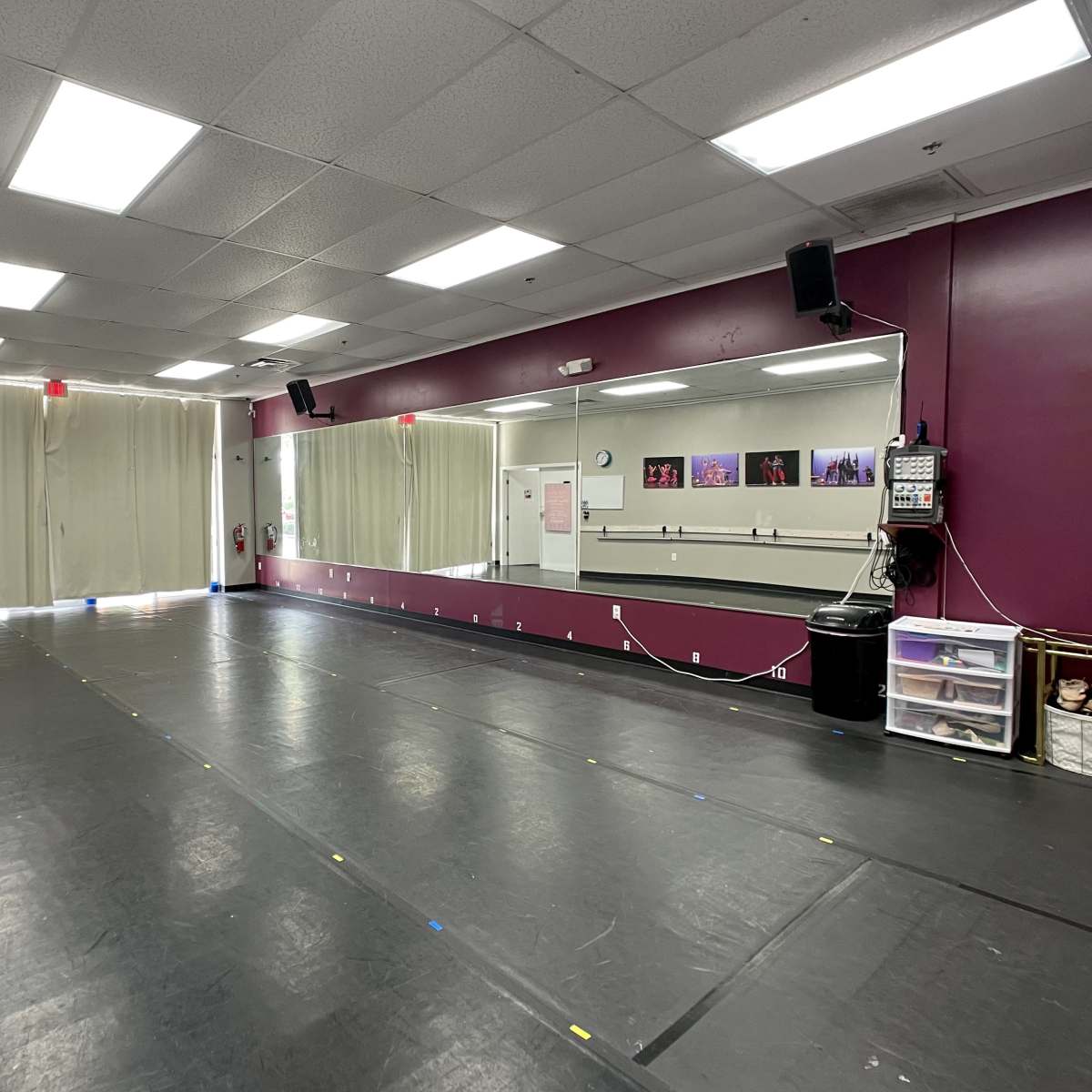 A spacious dance studio features a mirrored wall, wooden floors, and natural light coming through large windows.