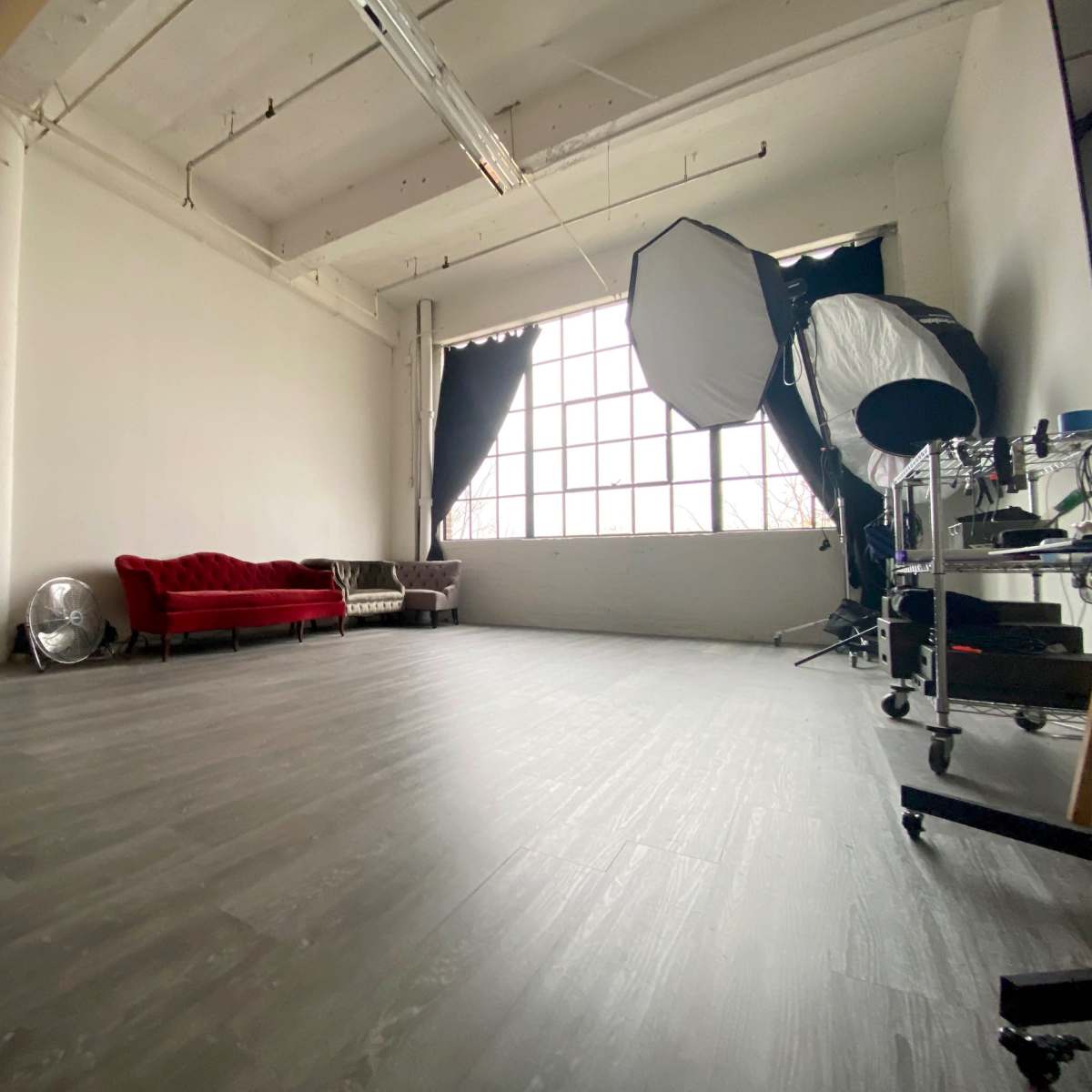 A spacious photography studio with a red velvet sofa, a large window, and various lighting equipment.