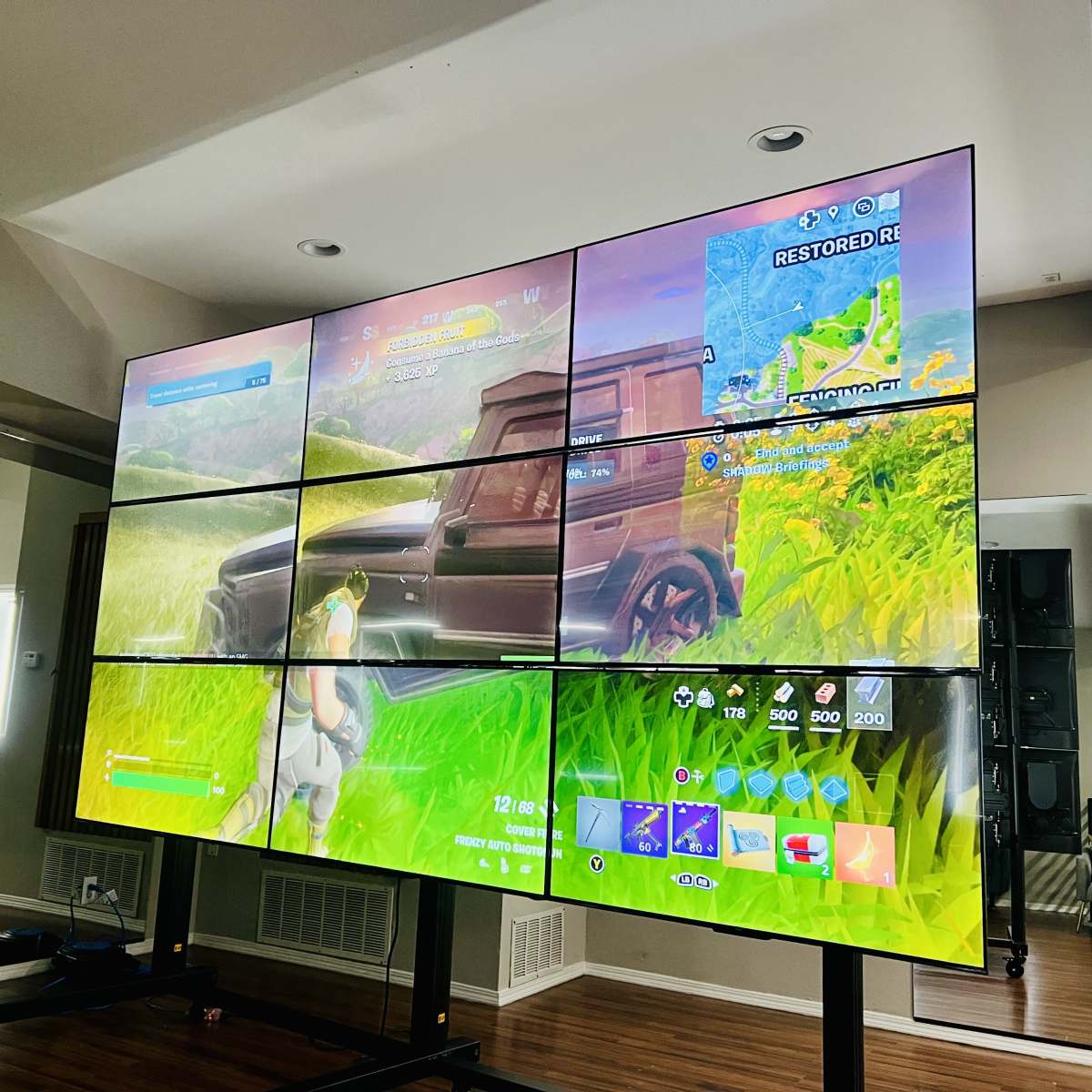 A large wall of screens displaying a gameplay scene from a video game, surrounded by a bright room with mirrors.