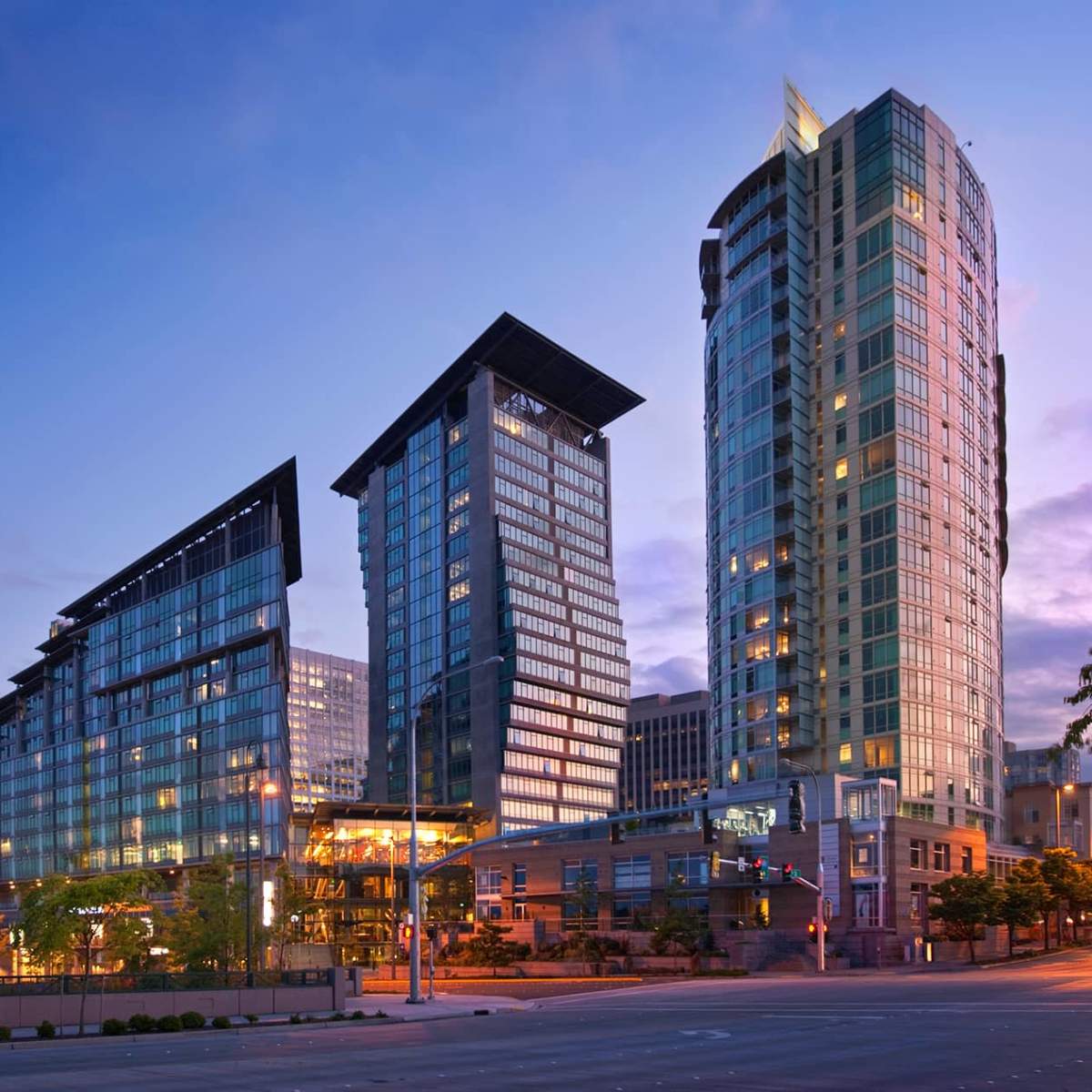 A modern urban skyline with three high-rise buildings, illuminated against a twilight sky.