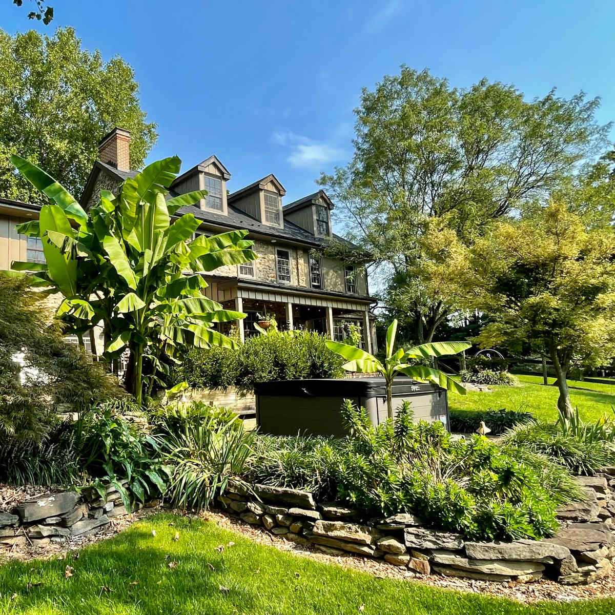 A large two-story house surrounded by lush greenery and several trees in a well-manicured lawn.