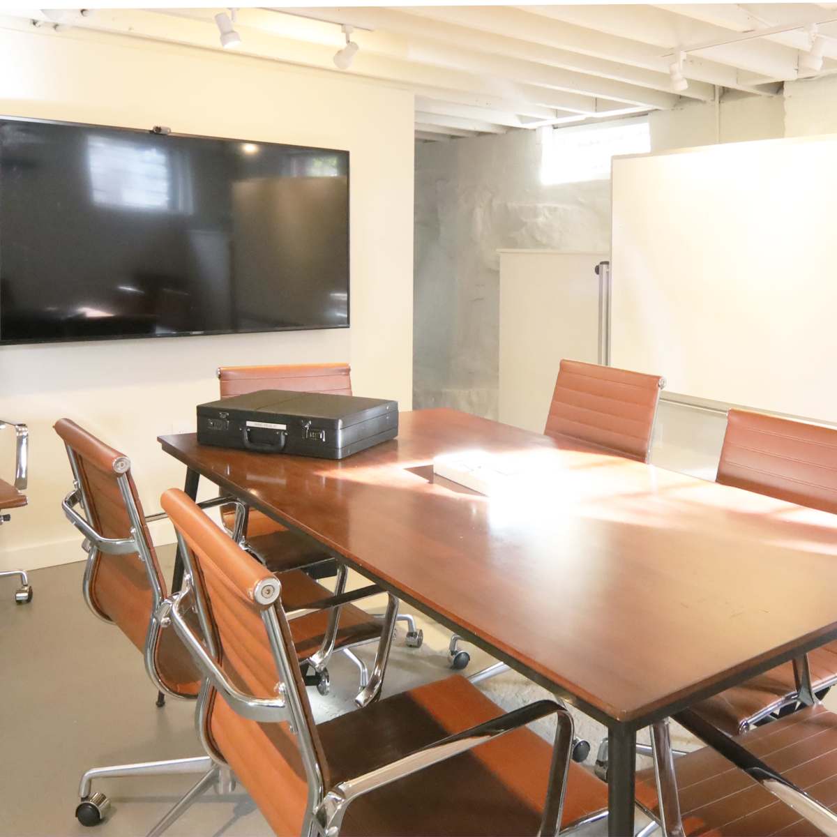 A conference room features a large table, brown leather chairs, a television screen, and a whiteboard.