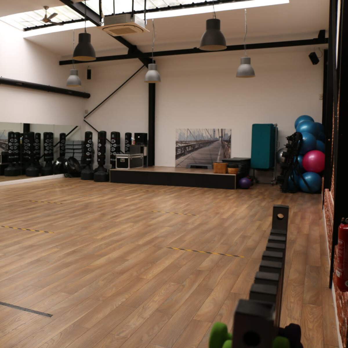 An empty fitness studio with wooden flooring, mirrors, and various workout equipment lined against the walls.