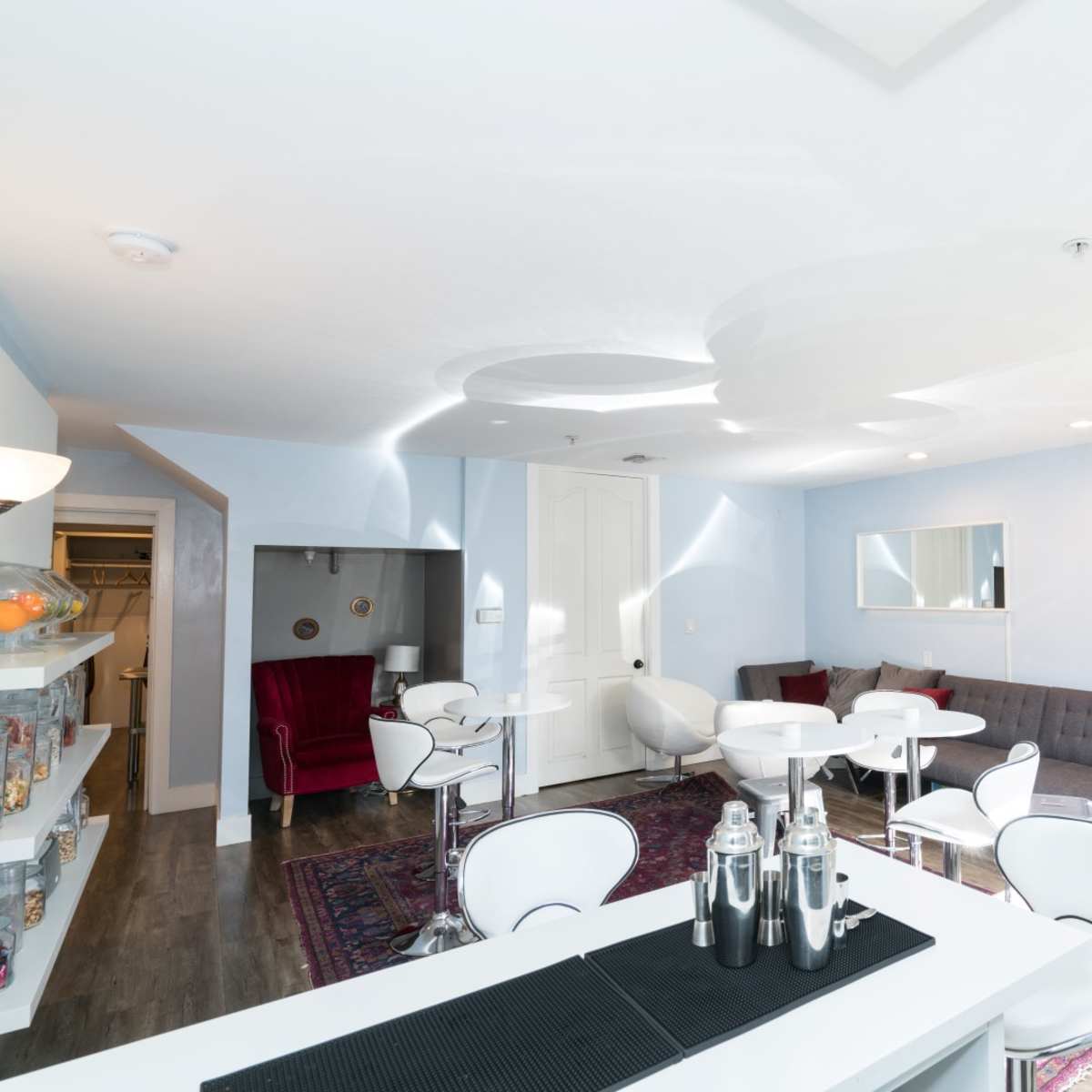 A modern lounge area with a gray sofa, white tables, and a sleek bar counter in a well-lit room.