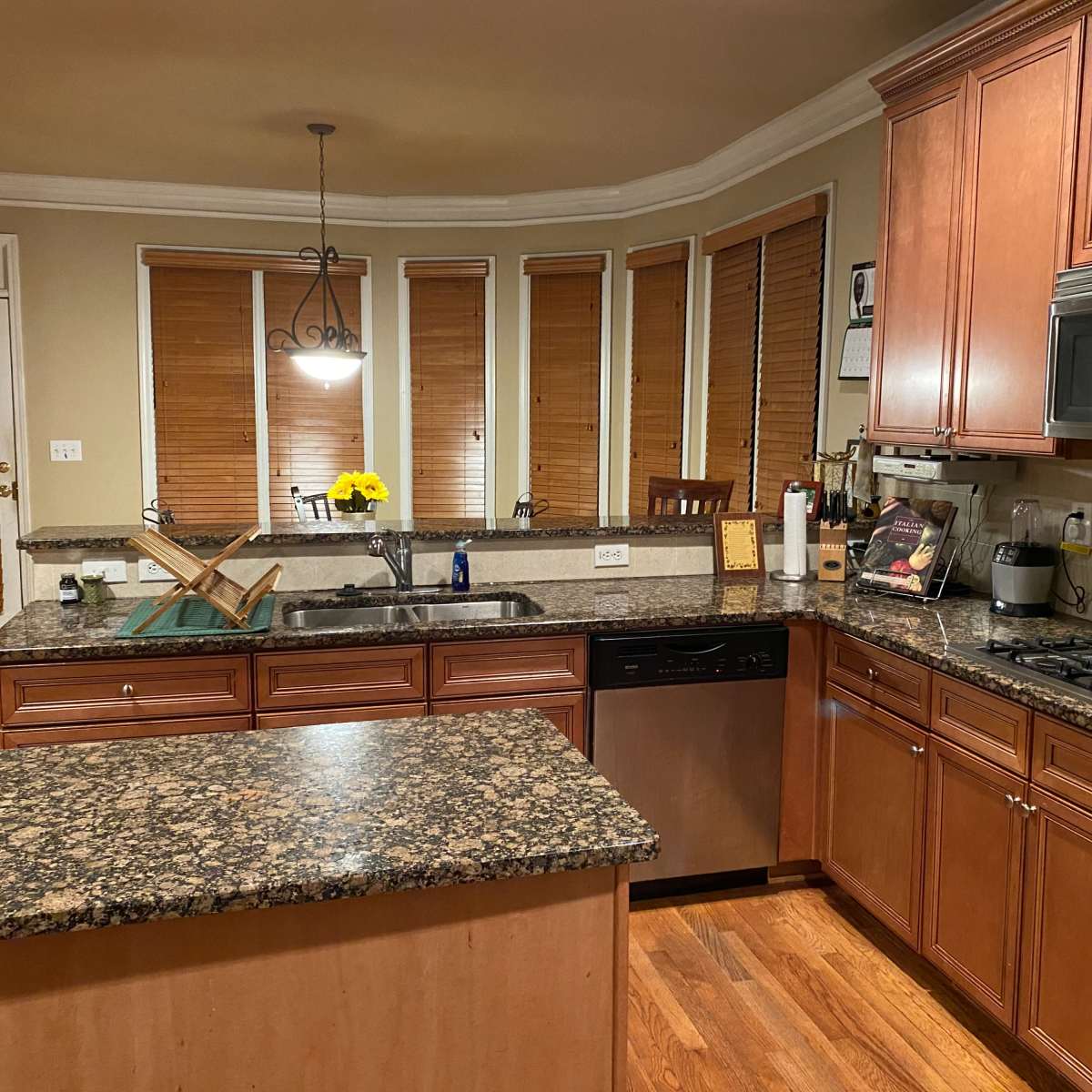 A modern kitchen with wooden cabinets, a granite countertop, and several windows covered by blinds.