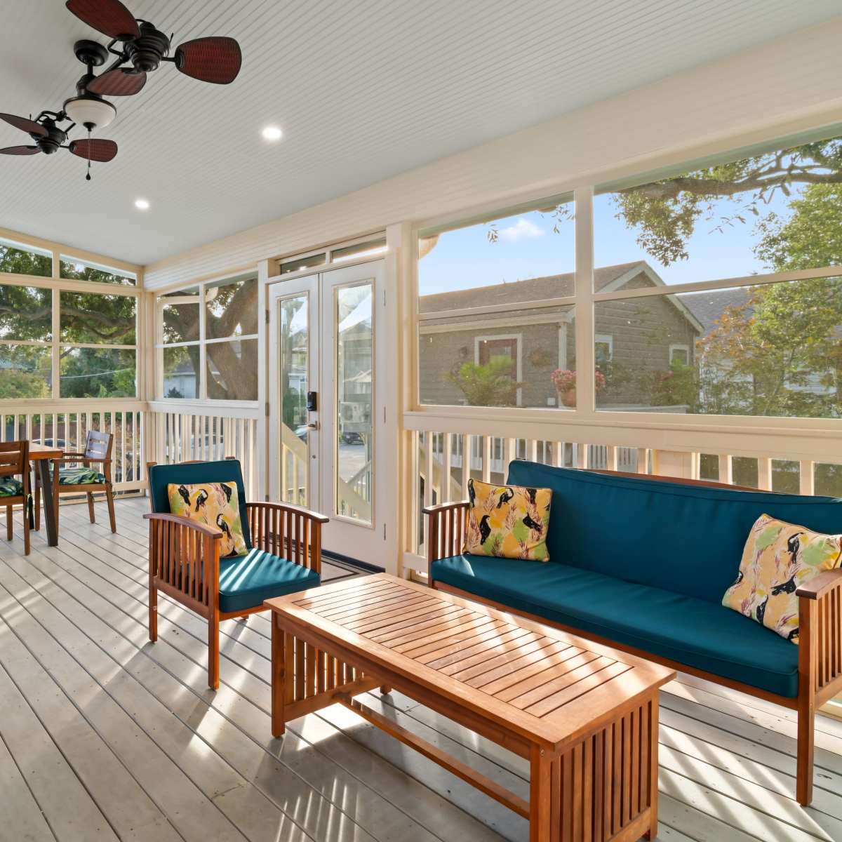 A spacious, screened-in porch featuring wooden furniture, including a seating area with blue cushions and a dining area with a table and chairs.